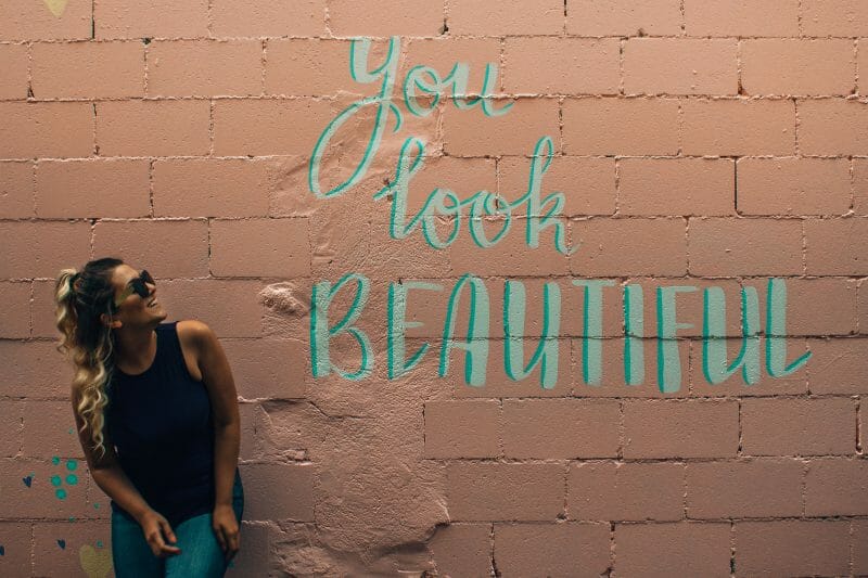 woman by a wall that reads ''you look beautiful''